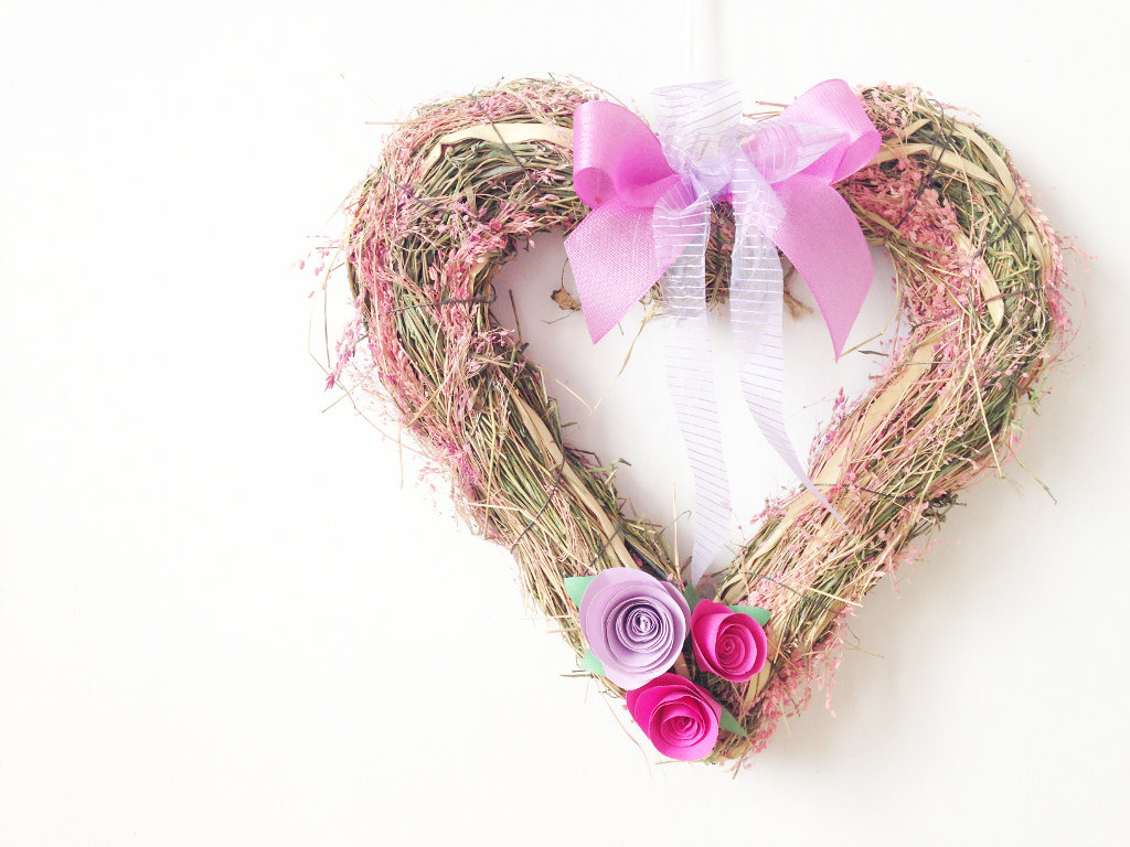 This image shows a DIY pink and lavender heart-shaped spring wreath with paper roses and ribbon bow