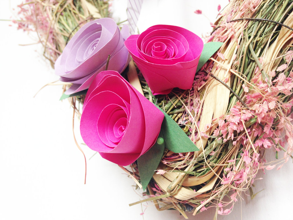 This image shows paper roses being fixed to a spring wreath in pink and lavender