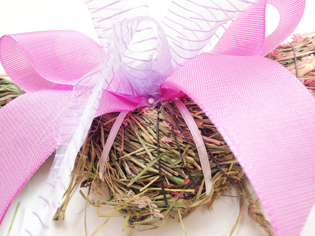 this image shows a pink and violet DIY ribbon bow attached to a straw spring wreath