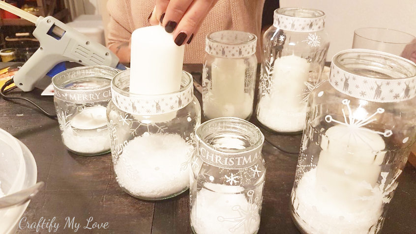 placing candle into snowflake painted recycled jar