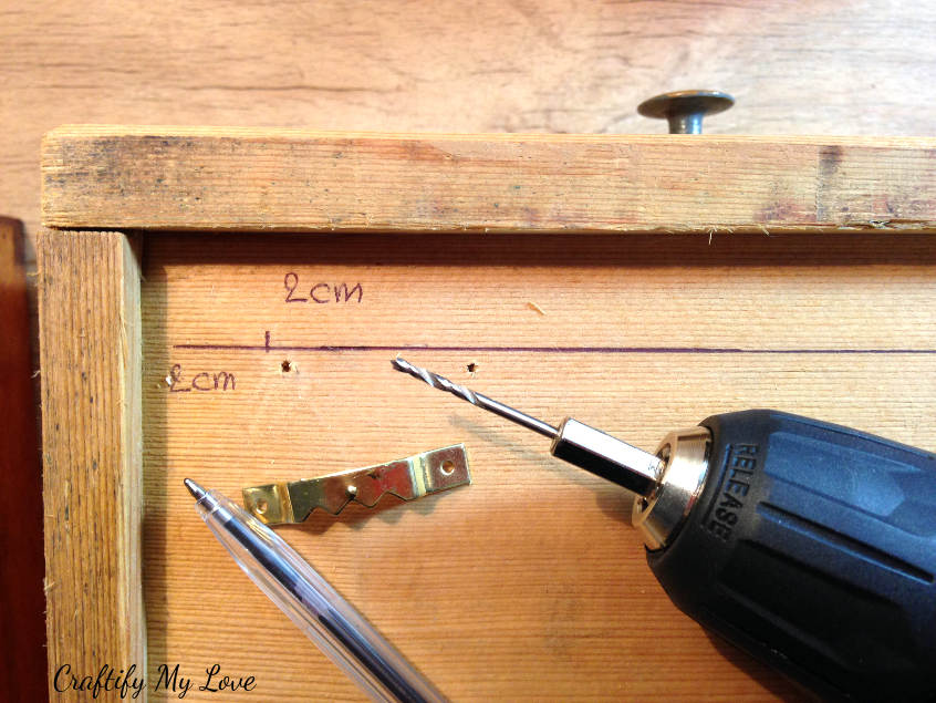 predrilling holes to fix sawtooth hanger to recycled drawer. This prevents wood from splintering.