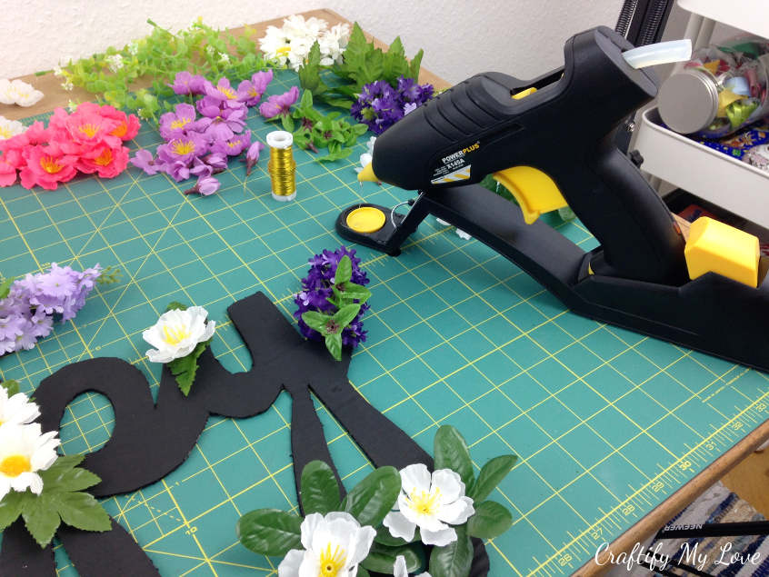 hotgluing flowers to chalkpaint covered cardboard sign