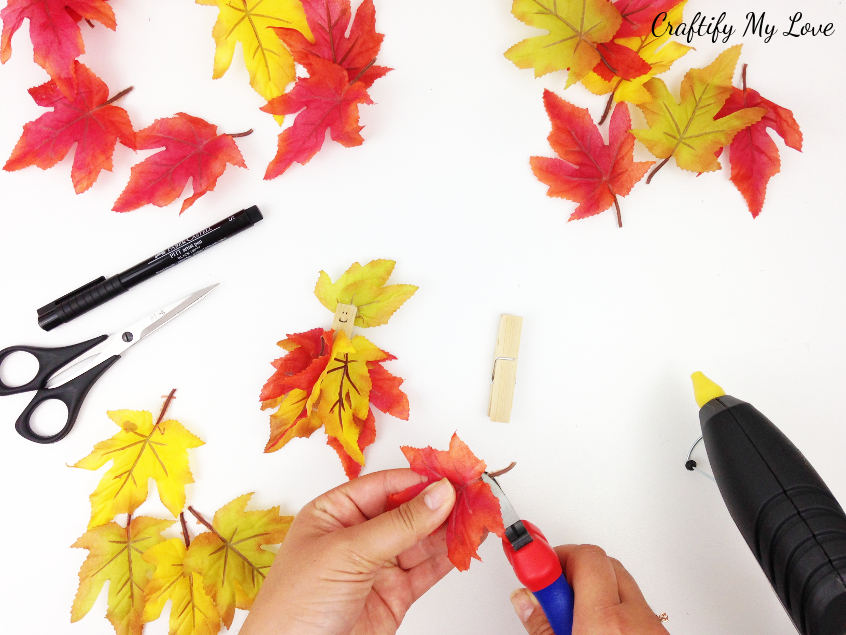 clipping off the stems of faux fall leaves for a fair craft that is suitable for kids and adults alike