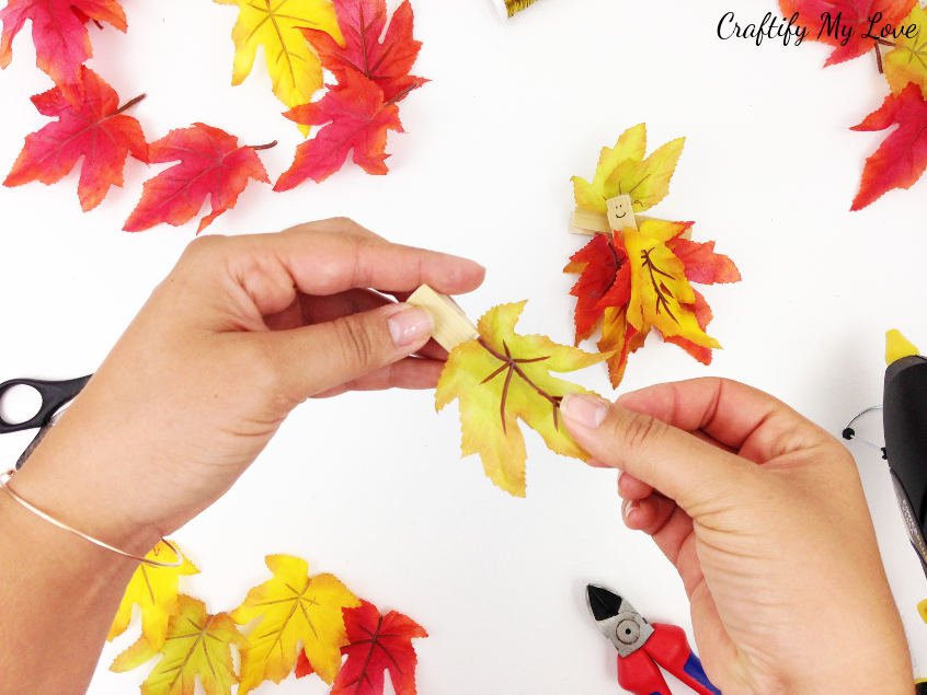 gluing faux fall leaf to clothes pin for fall kids craft project that can also be made as a flower fairy