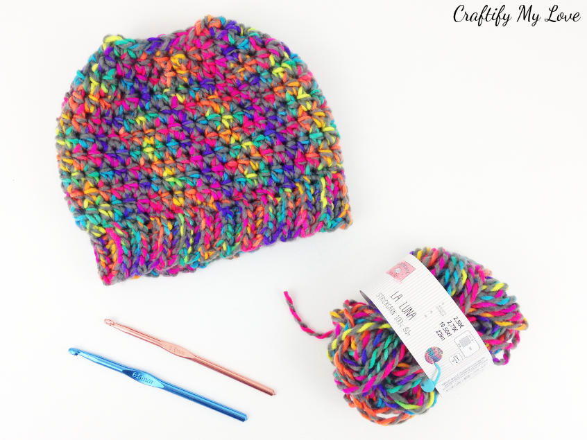 Supplies to make an easy crocheted rainbow messy bun hat for children.